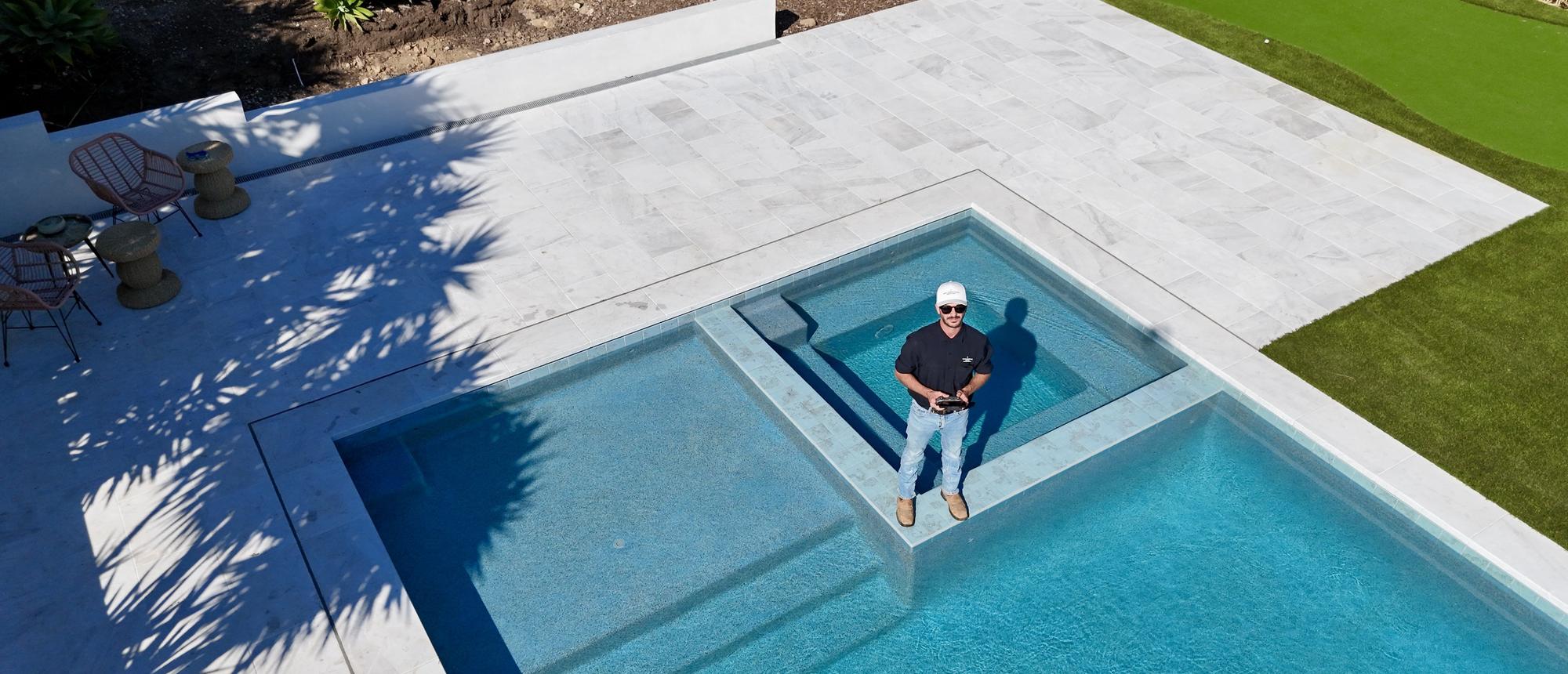 Aerial view of a pool, spa and stone deck with a putting green