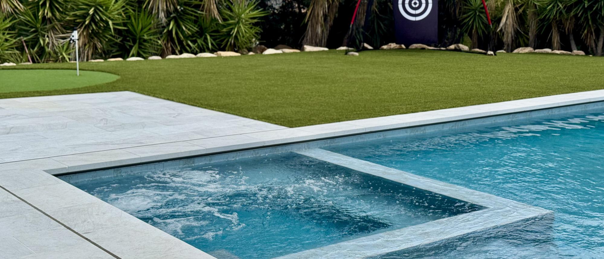 Pool and spa beside a putting green with palms behind