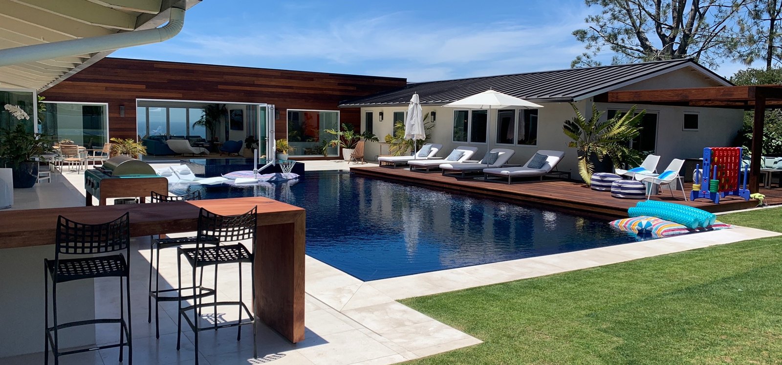 The same backyard finished: dark-finish pool, wood deck, loungers and outdoor kitchen