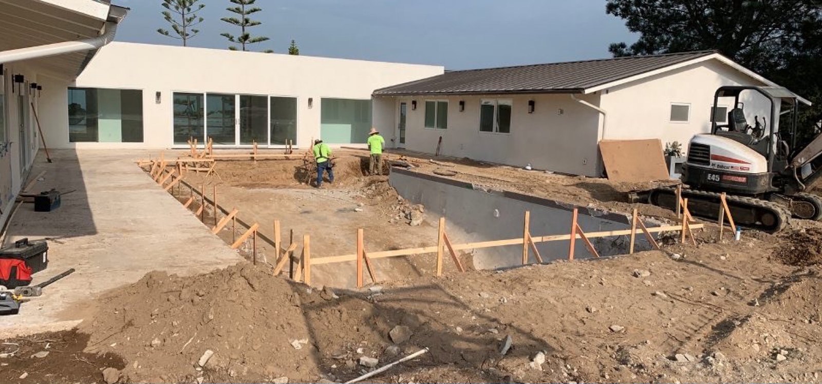 Backyard staked and excavated for a pool behind a modern house