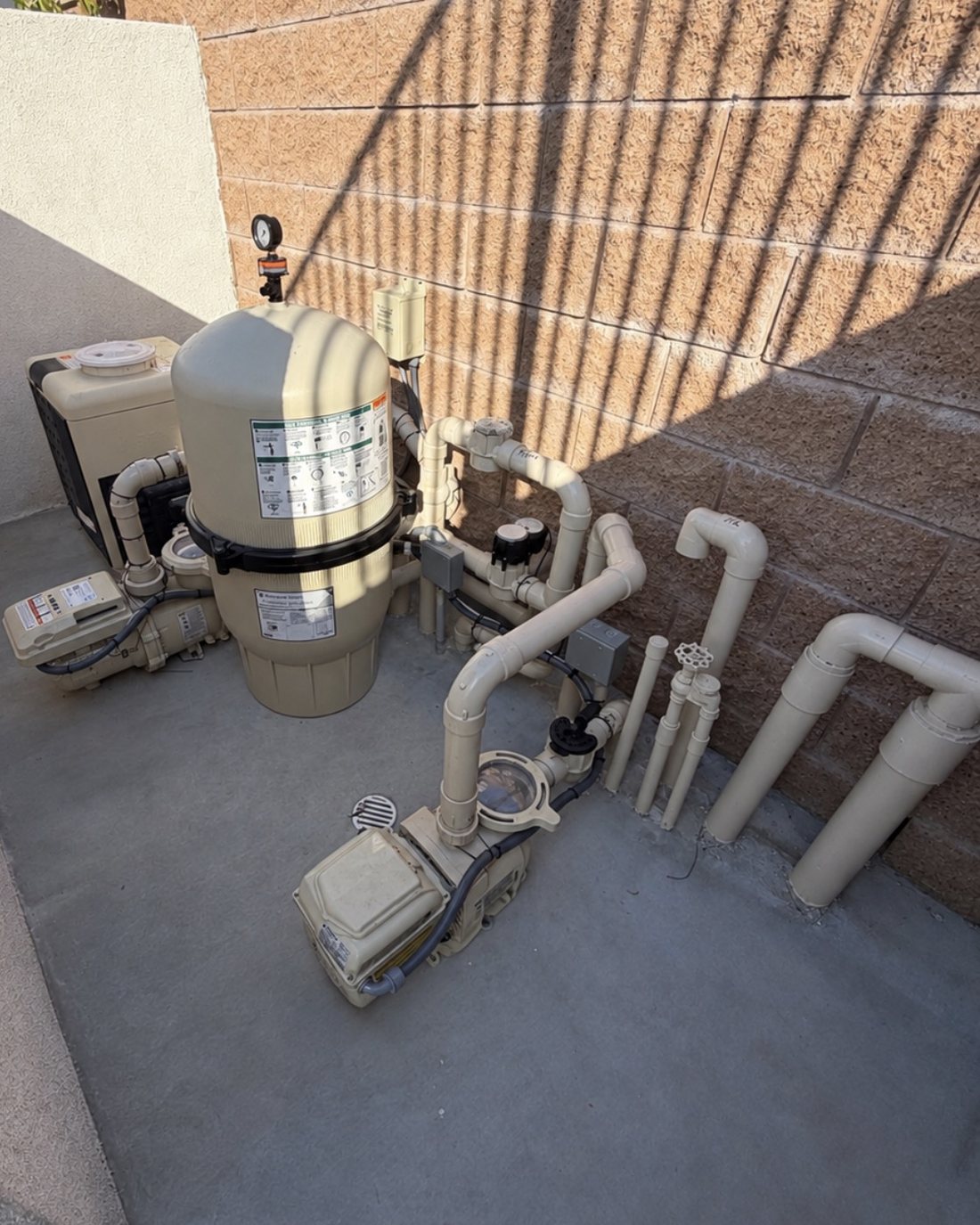 Pentair equipment pad: heater, cartridge filter and two pumps on a concrete pad against a block wall