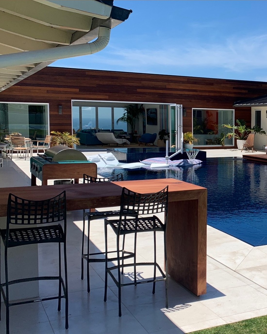 Outdoor kitchen with bar seating beside a finished pool and wood deck