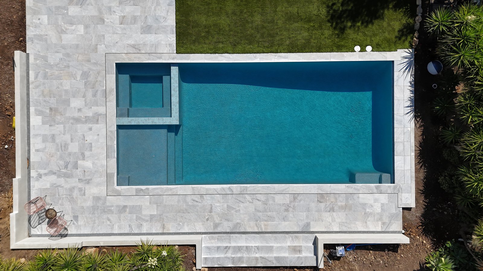 Geometric pool with raised spa and bench, marble-look paving and lawn, seen from above