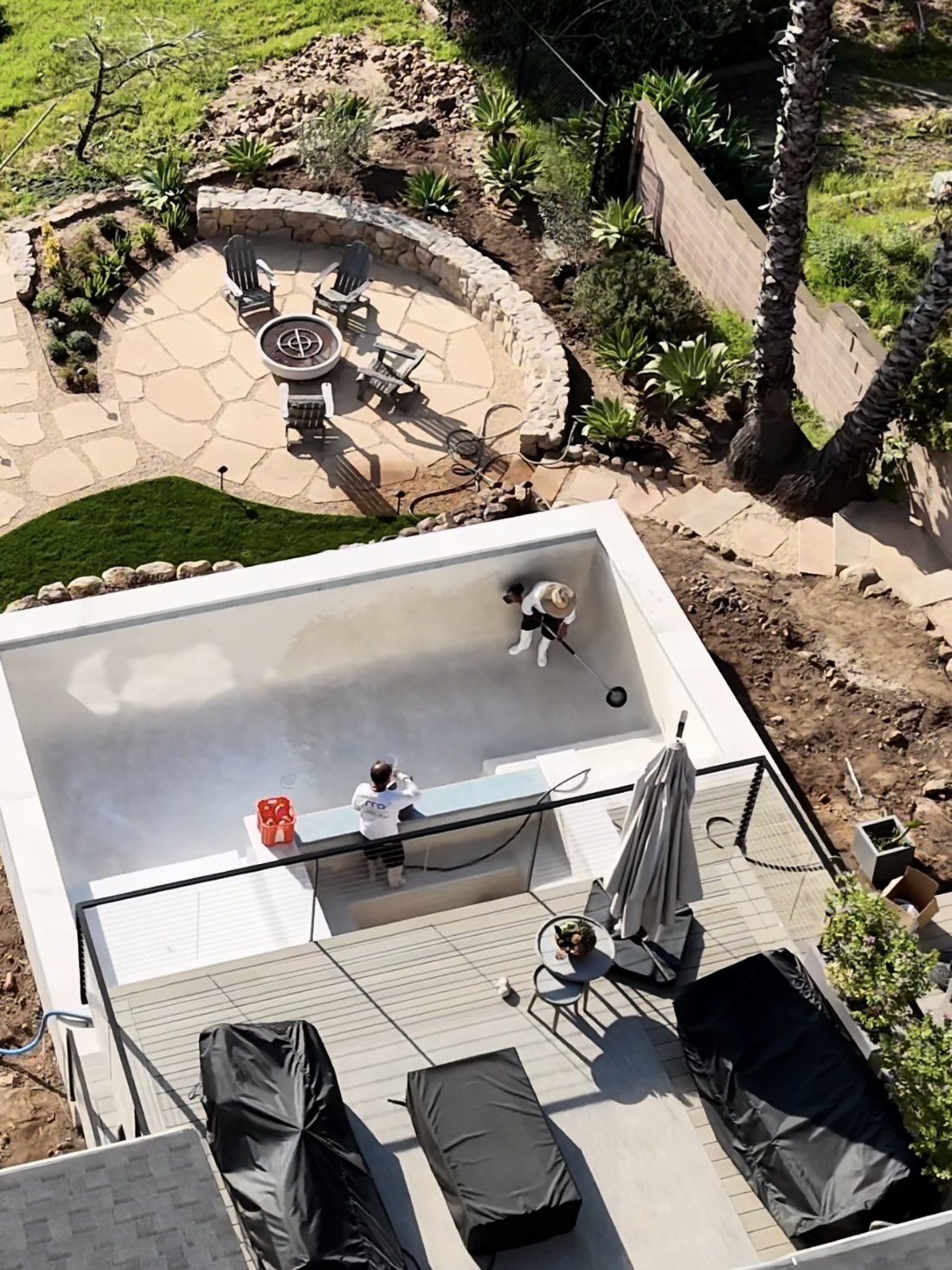 Crew finishing the interior of a new pool below a stone fire-pit patio