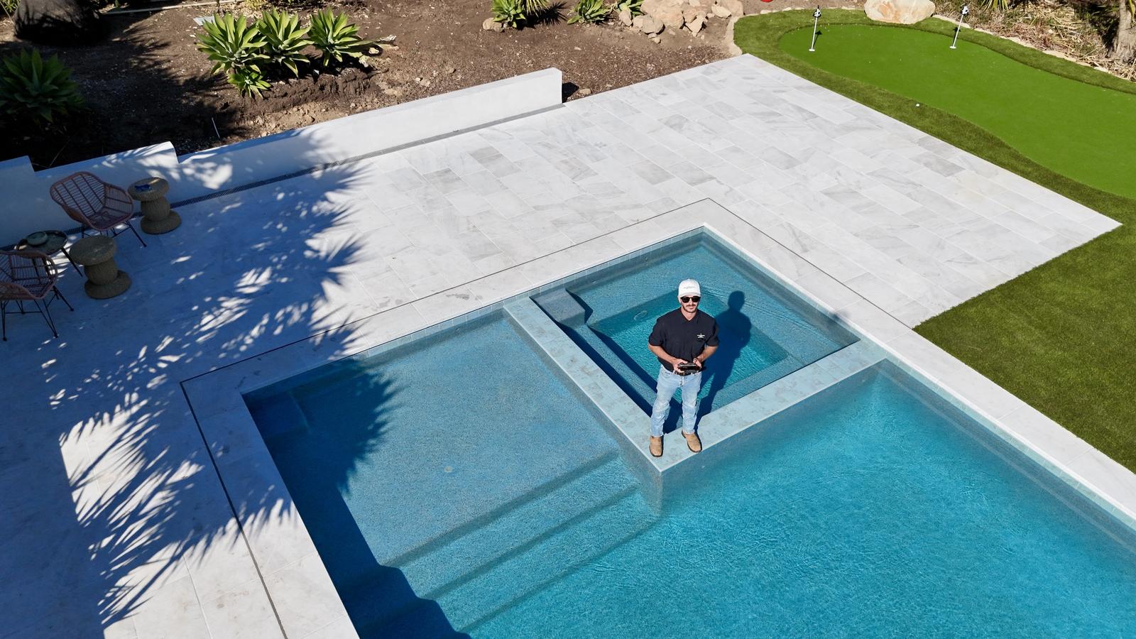 Aerial view of a pool, spa and stone deck with a putting green