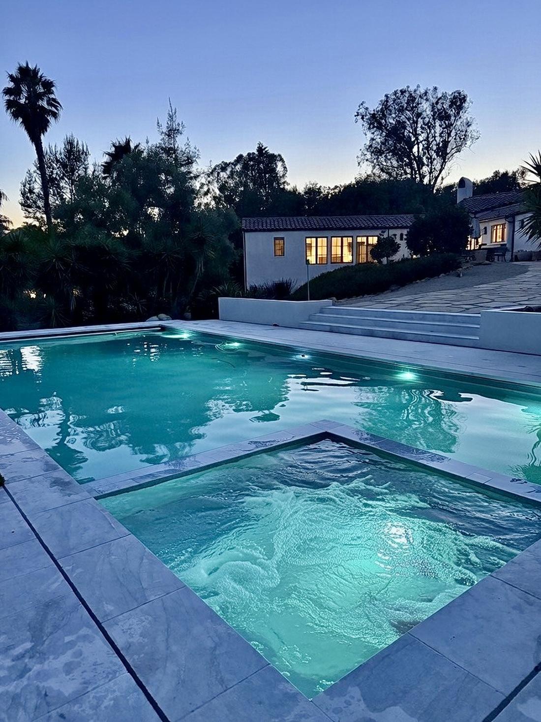 Pool and spa lit at dusk with the house behind
