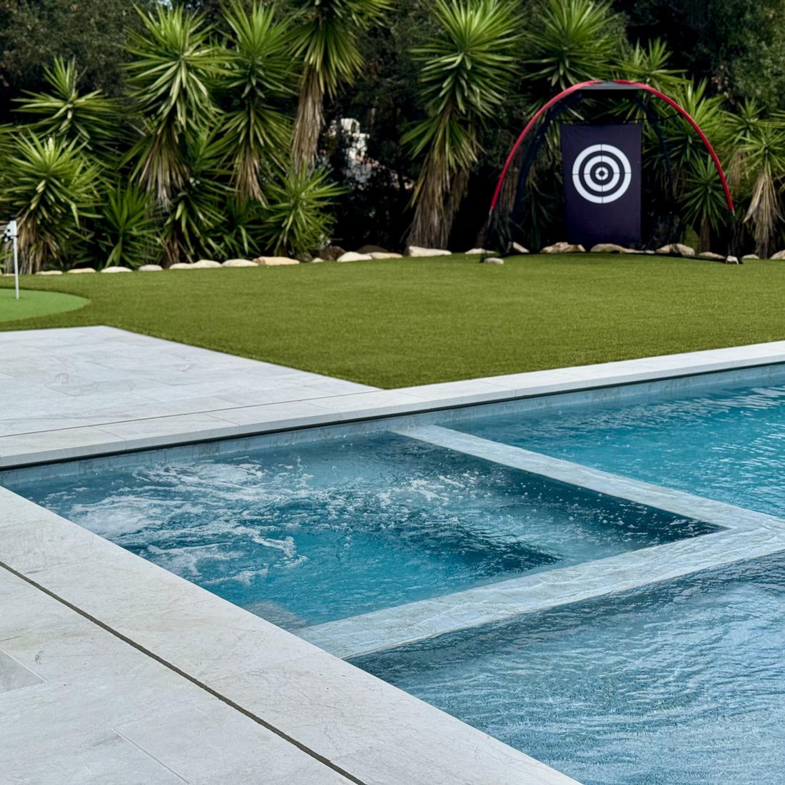 Pool and spa beside a putting green with palms behind