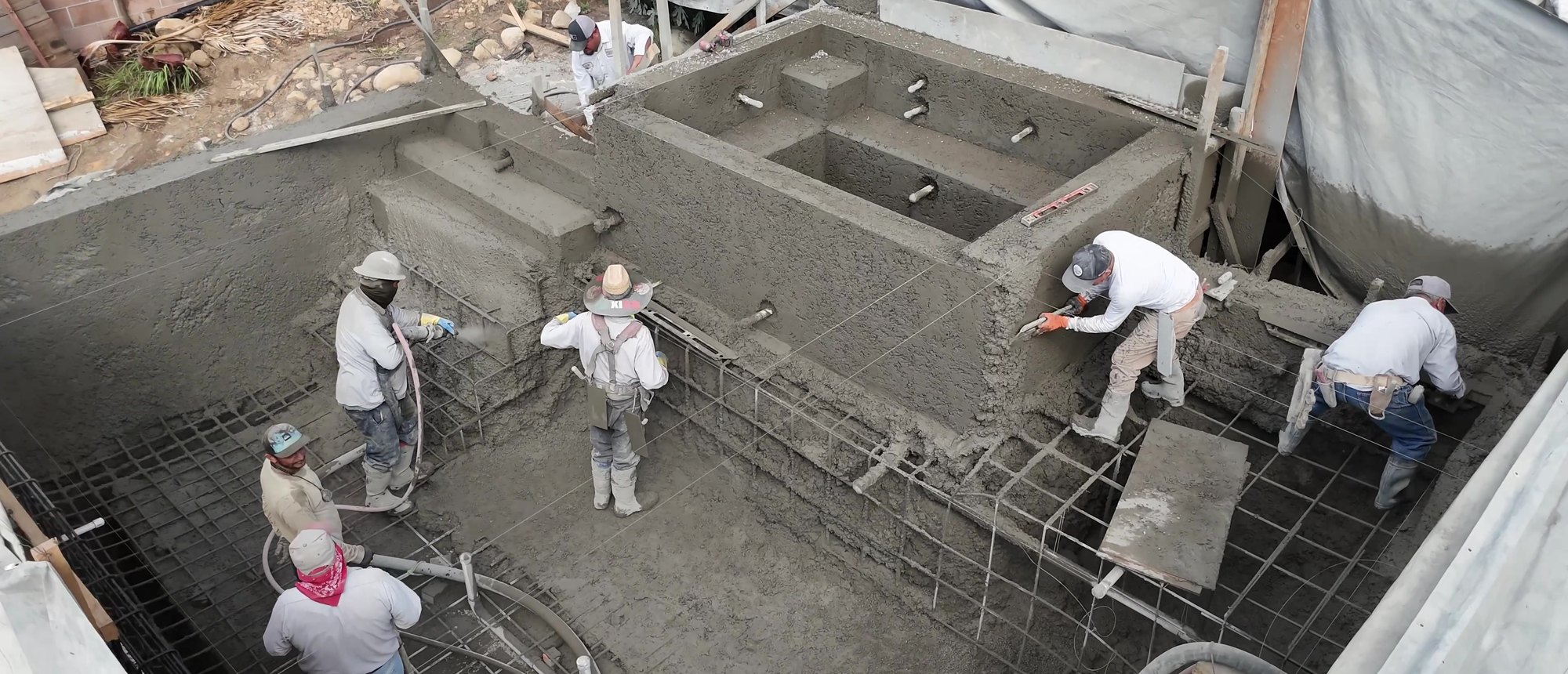 Crew shooting shotcrete over the steel of a new pool shell, seen from above