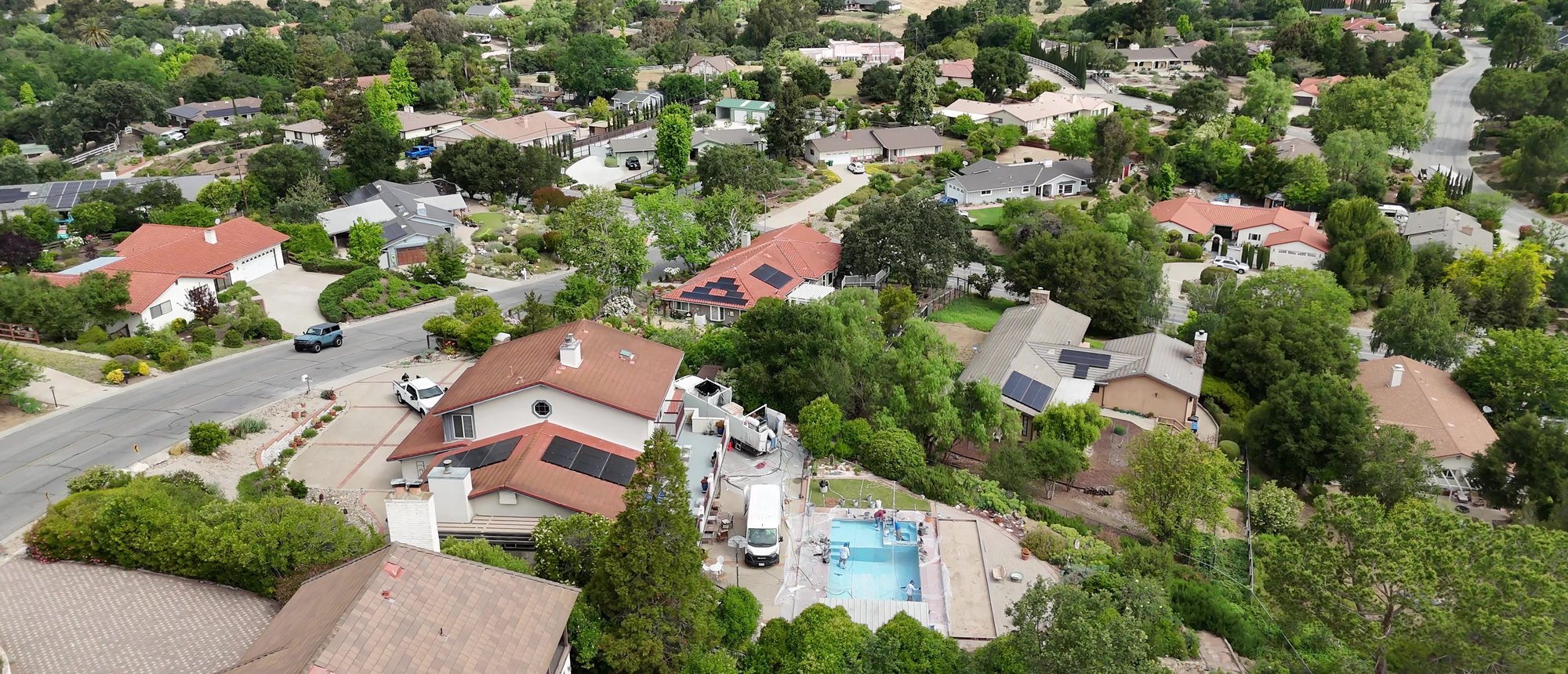 Finished pool and spa behind a home on a hillside street, seen from the air