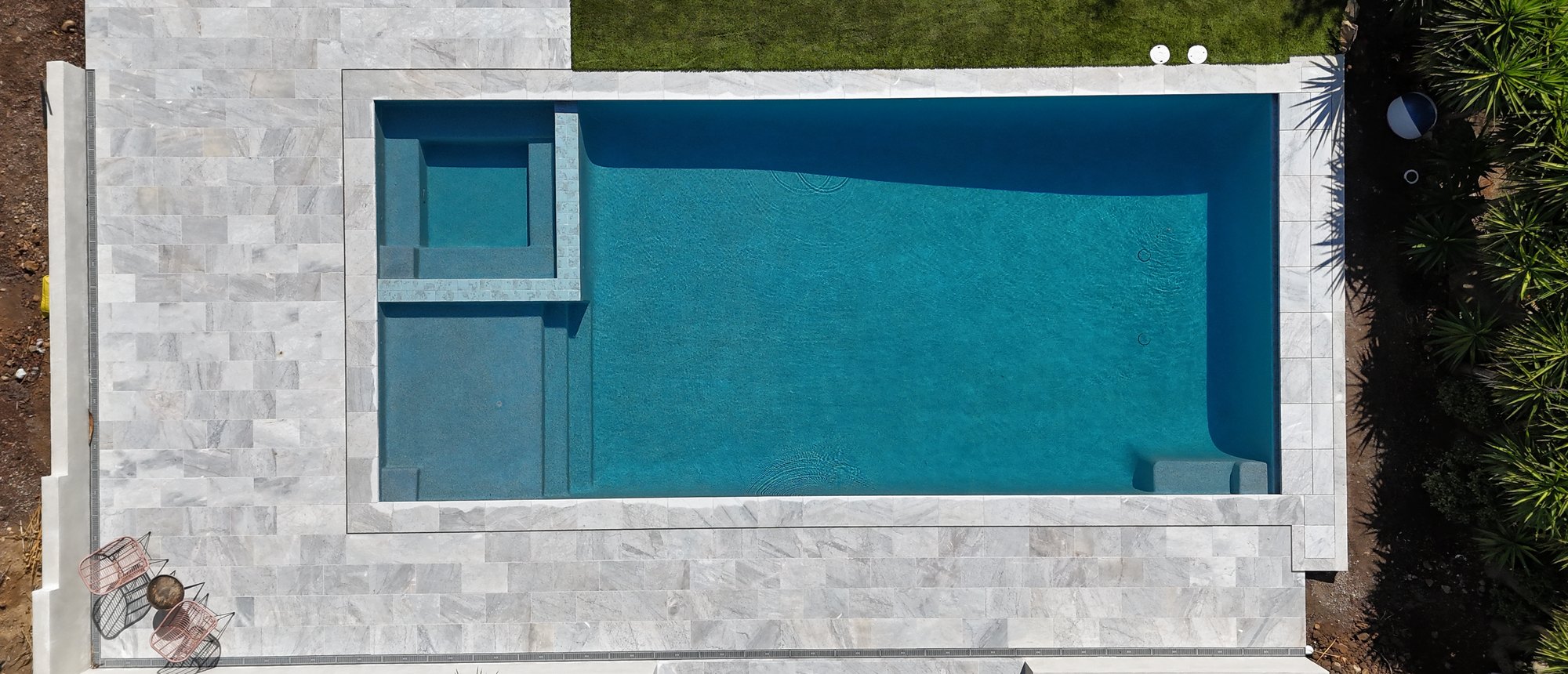 Geometric pool with a raised spa, bench and Baja shelf, marble-look paving, seen from above